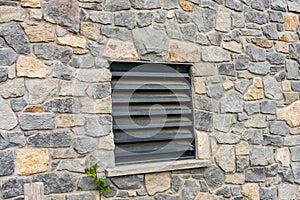 Window of a house closed with black wooden shutters. Old, ancient wood window with blind or shutters. Stone home facade