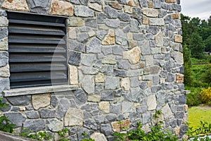 Window of a house closed with black wooden shutters. Old, ancient wood window with blind or shutters. Stone home facade