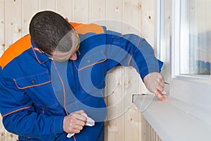 The window installer seals up the cracks with white silicone, smearing them clean with a cloth