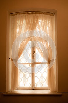 The window with lace grating and delicate tulle is light yellow-pink in color.