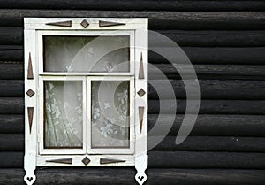 The window of a log country house is decorated with a simple pattern