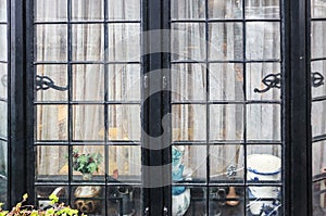 Window of modest homey home - broken black metal bay window with net curtains and knick-knacks sitting inside photo