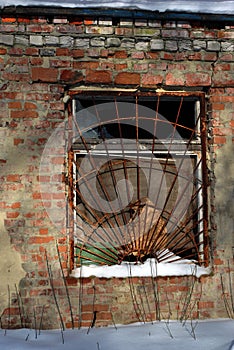 The window of the old brick building covered with rusty iron grate, winter street, grunge background