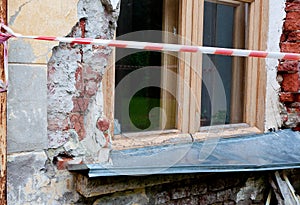 Window on old broken wall with visible bricks behind the red and white warning tape
