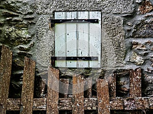 The window of an old European country house with walls of stones and a wooden fence