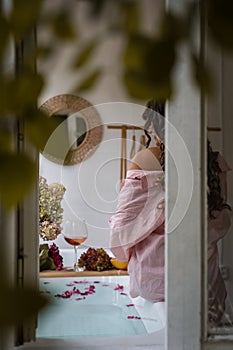 Window outside view of the bath tub, grapefruit slices, bunch of grapes, a glass of wine and a woman, selective focus