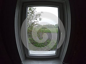 Window with a plastic frame. Window view of a simple village garden on a rainy day. Fish eye effect