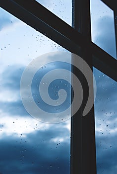 Window with rain droplets with view on dark blue cloudscape