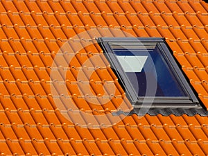 Window on roof of house with orange roof tiles on a background of blue sky
