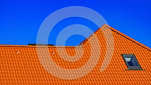 Window on roof of house with orange roof tiles on a background of blue sky