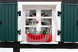 Window sill with Christmas decoration in red flower box. Small Christmas tree, red ball, red and white candy cane, green shutters. photo