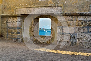 Window in a stone wall showing the sea and a boat photo