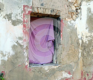 The window of a very old collapsed abandoned house hung with a pink rag,