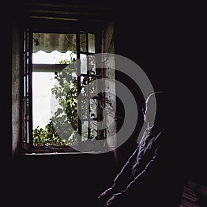 Window view from inside an old uninhabitable house and a blurred silhouette of a man. Depression, loneliness, despair, decline,