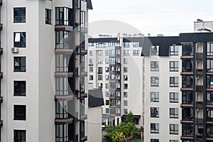 Window view of modern white apartment buildings with black roofs on a cloudy day. Cozy residential complex
