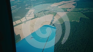 Window view of a small propeller aircraft making a turn in air flight above rural airfield