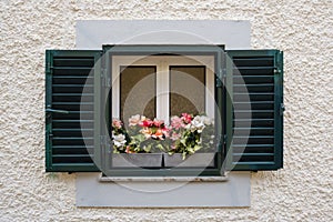 window in the wall with blinders open and a vase with flowers