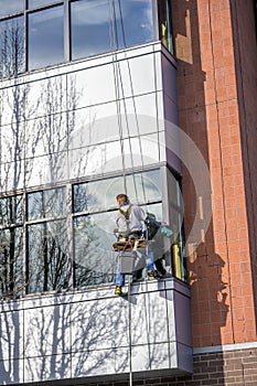 Window washer in working outfit washes windows in a multi-storey modern building