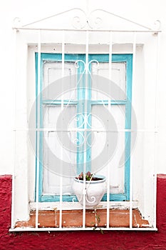 Window with white bars and pots with geraniums