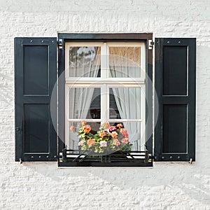 Window on white brick wall closeup with shutters and blooming flowers pot