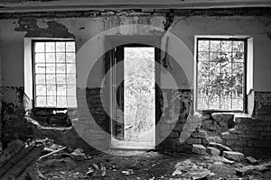 Windows with bars and an open door of an abandoned building from the inside black and white photo