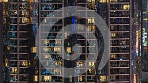 Windows of the multi-storey building of glass and steel lighting inside and moving people within