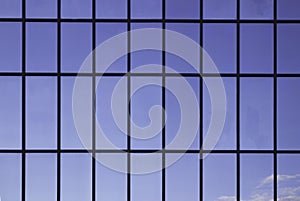 Windows in an office building, background. Blue sky reflected in the glass, black frames