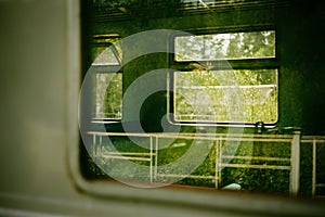 The windows of an old electric train reflecting the greenery of trees. The experience of traveling on public transportation amidst