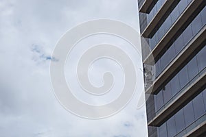 A windows washer doing his job at high modern skyscraper corner with cloudy sky