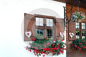 The windows of the wooden house are beautifully decorated with white hearts and flowers