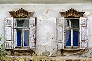 Windows with wooden shutters and carved platbands of an old dilapidated house with cracked plaster