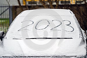 Windscreen wipers and a snow covered car, 2023 inscription. handwritten on snowy window