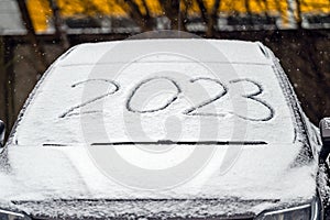 Windscreen wipers and a snow covered car, 2023 inscription. handwritten on snowy window