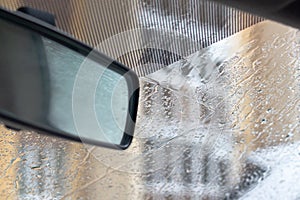 The windshield of a white car is covered with water droplets during rain