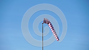 Windsock with red and white stripes show direction of wind blowing and speed. Cone wind indicator develops on blue sky background