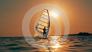 Windsurfer is crossing the sea in the setting sun