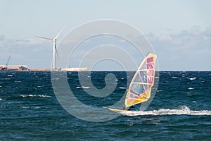 A windsurfer is sailing in Pozo Izquierdo, town of Gran Canaria island with a wind turbine in the background