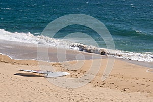 Windsurfing board lying on sandy beach on sunny day in summer with ocean waves