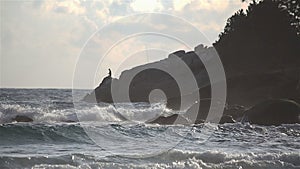 Windy sea wave crashing coast rocks during sunset with fisherman in background