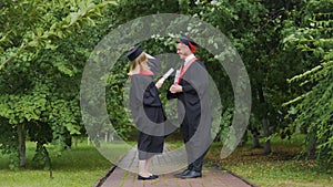 Windy weather, pair of graduates standing in park with diplomas, wind of change