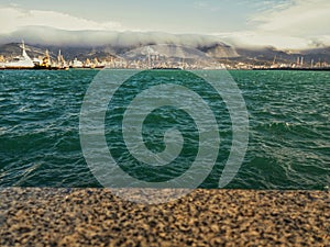 Windy weather at sea, waves. Industrial port, sea transport. Mountain range and flying clouds.