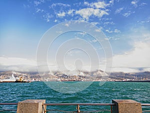 Windy weather at sea, waves. Industrial port, sea transport. Mountain range and flying clouds.