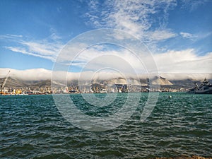 Windy weather at sea, waves. Industrial port, sea transport. Mountain range and flying clouds.