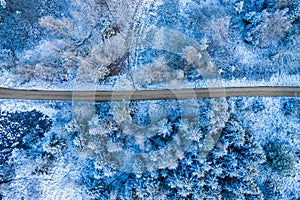 Windy winter road in snow covered forest, top down aerial view.