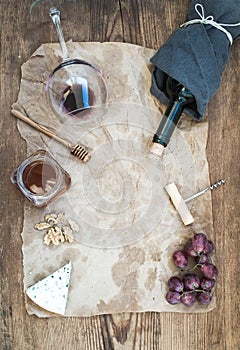 Wine and appetizer set with copy space in center. Glass of red wine, bottle, corkscrewer, blue cheese, grapes, honey