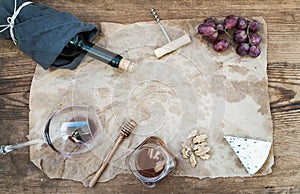 Wine and appetizer set with copy space in center. Glass of red wine, bottle, corkscrewer, blue cheese, grapes, honey