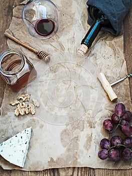 Wine and appetizer set with copy space in center. Glass of red wine, bottle, corkscrewer, blue cheese, grapes, honey