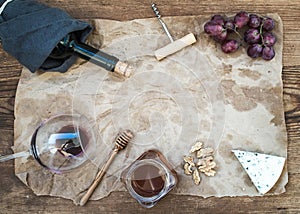 Wine and appetizer set with copy space in center. Glass of red wine, bottle, corkscrewer, blue cheese, grapes, honey