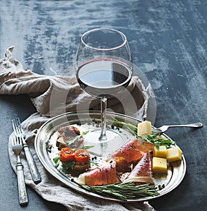 Wine appetizer set. Glass of red wine, vintage dinnerware, brushetta with cherry, dried tomatoes, arugula, parmesan, smoked meat