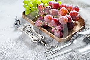 Wine background. A branch of green and red grapes, an empty bottle, a corkscrew and a cork. Concept of home winemaking. White